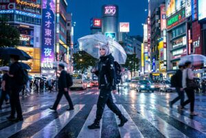 Yuki walking across a rainy Shibuya crossing in Neo-Tokyo under transparent umbrella with city neon reflections